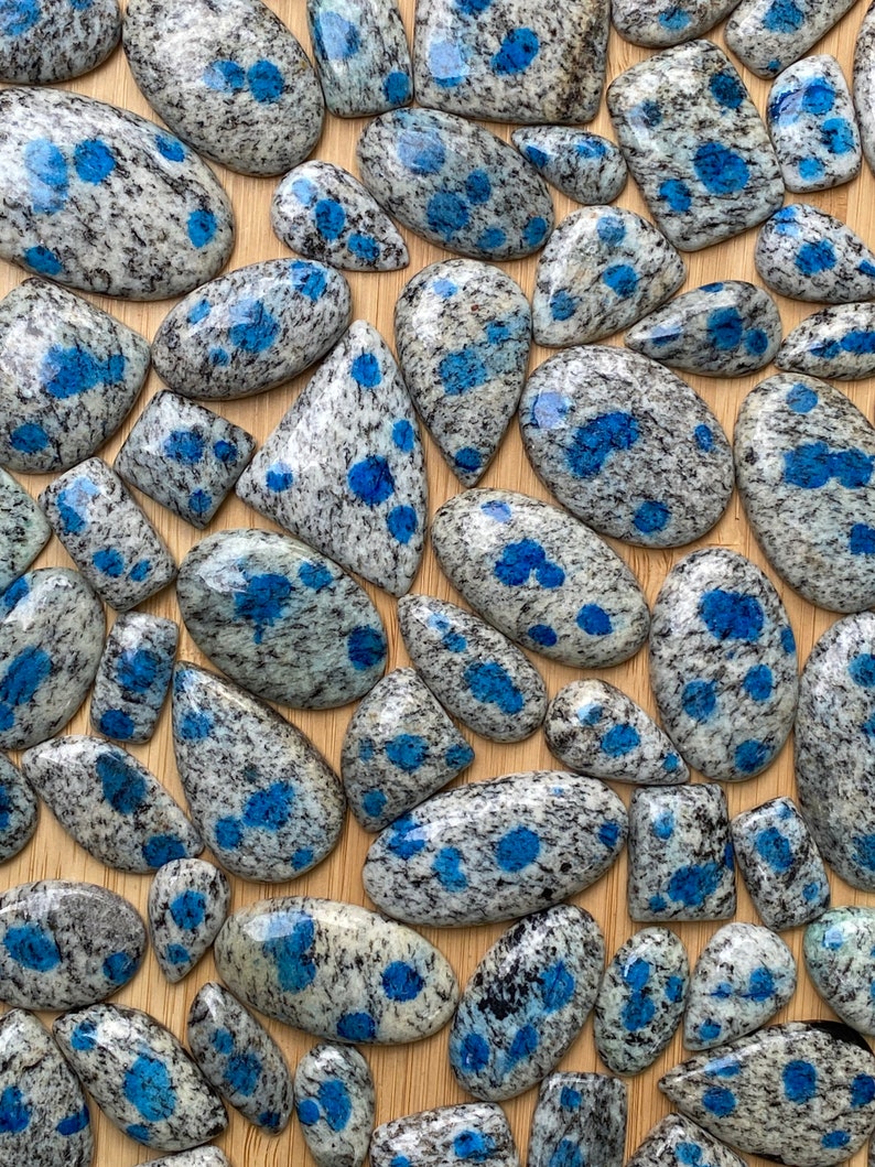May include: A collection of blue and gray speckled gemstone cabochons. The stones are various shapes and sizes, and have a unique speckled pattern.