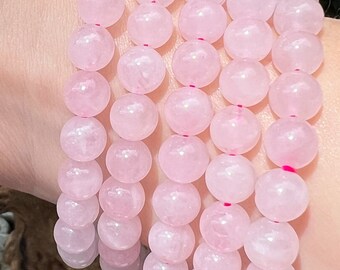 May include: A set of six pink rose quartz bracelets with round beads. The bracelets are stacked on a person's wrist.