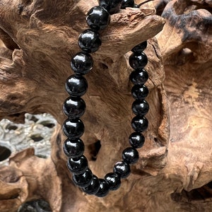 Puede incluir: Un brazalete negro de cuentas con un acabado brillante. El brazalete está hecho de cuentas redondas y está enhebrado en un cordón negro.