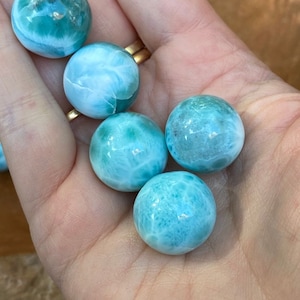 May include: A collection of five blue and green ocean jasper spheres, also known as sea jasper, in various sizes. The spheres are smooth and polished, with a swirling pattern of blue, green, and white.