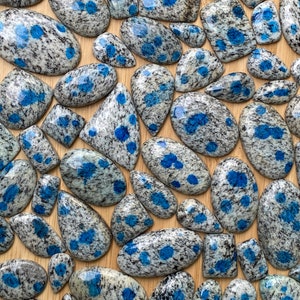 May include: A collection of polished blue and gray speckled stones. The stones are various shapes and sizes, and have a speckled pattern of blue and gray.