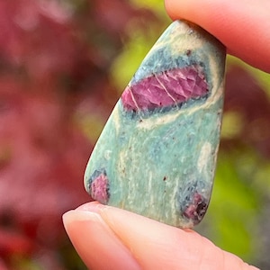 May include: A green and pink gemstone with a triangular shape. The gemstone has a mottled pattern of green and pink.
