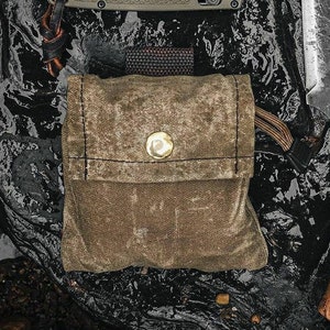 May include: A small, brown canvas pouch with a flap closure and a brass button. The pouch has a worn, vintage look and is perfect for carrying small items.