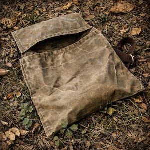 May include: A brown waxed canvas messenger bag featuring a rectangular flap closure, a main compartment, and a dark brown adjustable strap with a metal buckle. The fabric displays a weathered, creased texture throughout the exterior surface.