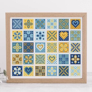 May include: A framed cross-stitch sampler featuring a grid of 25 squares. Each square displays a unique geometric pattern in shades of blue and yellow, including hearts, flowers, and crosses. The wooden frame adds a rustic touch to the artwork.