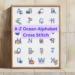May include: A framed cross-stitch sampler featuring the alphabet with an ocean theme. Each letter is represented by a marine-related image, such as an anchor, boat, or seahorse. The text "A-Z Ocean Alphabet Cross Stitch" is displayed in a purple banner.