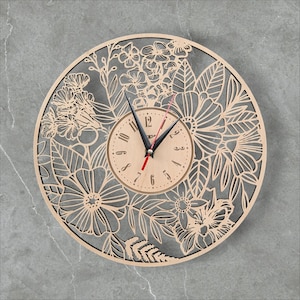 May include: A round wooden wall clock with a floral design. The clock face is light brown with black numbers and black clock hands. The outer ring features a laser-cut floral pattern. The second hand is red.