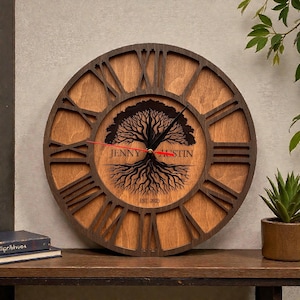 Könnte beinhalten: Wanduhr aus Holz mit einem Lebensbaum-Design. Die Uhr hat römische Ziffern und einen dunkelbraunen Rahmen. Das Zifferblatt trägt die Namen "JENNY AUSTIN" und das Jahr "EST. 2025". Die Zeiger der Uhr sind rot.