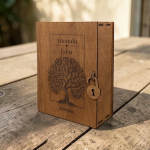 May include: A rectangular wooden box with a hinged door featuring a laser-engraved tree design, the names Amanda and John, and the date 25/08/2026. A small wooden padlock-shaped latch is attached to the front, securing the door of the box.