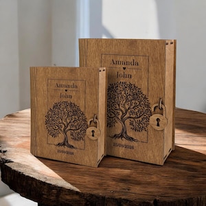 May include: Two wooden keepsake boxes with a tree design and the names "Amanda" and "John" engraved on the front. The boxes have a lock and key closure. The date "25/08/2026" is also engraved on the front of the boxes. The boxes are on a wooden surface.