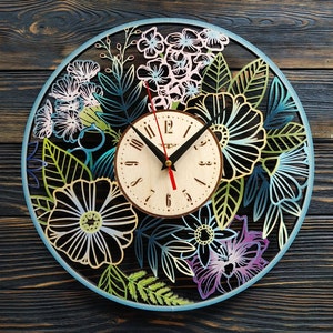 K&ouml;nnte beinhalten: Dekorative Wanduhr aus Holz mit floralem Design. Die Uhr hat ein helles Zifferblatt mit schwarzen Zeigern und einem roten Sekundenzeiger. Der &auml;u&szlig;ere Rahmen ist hellblau, und die floralen Ausschnitte sind in Gr&uuml;n-, Blau- und Lilat&ouml;nen gehalten. Durchmesser: ca. 30 cm.