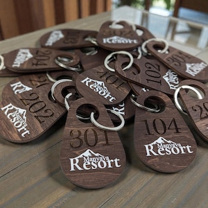 May include: A selection of wooden key fobs with silver key rings. Each fob is engraved with a room number and the "Manyava Resort" logo in white. The key fobs are a dark brown colour.