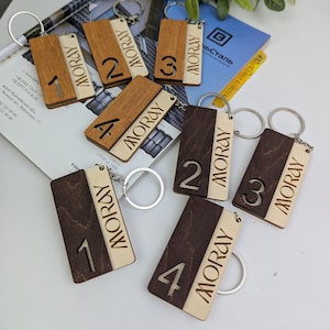 May include: A collection of wooden keyrings, each engraved with the name "MORAY" and the numbers 1, 2, 3, and 4. The keyrings feature a two-tone design, with light and dark wood sections. They are attached to silver key rings.
