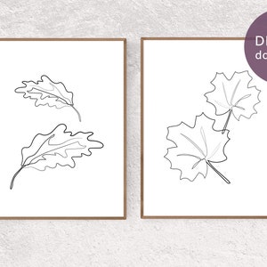 May include: Two printable art prints featuring minimalist line drawings of leaves. The prints are in black and white and are framed in a light brown wood frame.