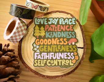 May include: A colorful sticker with the words "Love Joy Peace Patience Kindness Goodness Gentleness Faithfulness Self Control" is displayed on a wooden slice. Decorative washi tape rolls with fern, butterfly, and checkered patterns are also present.