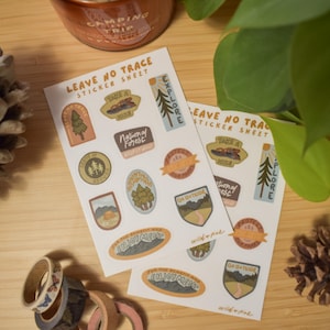 May include: Two sheets of stickers with a Leave No Trace theme. The stickers feature illustrations of trees, mountains, and other nature-inspired designs. The stickers are printed on white paper with a brown background.