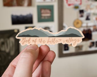 May include: A sticker with a mountain range design and the text "God of the hills + valleys".