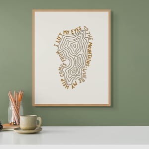 May include: A beige framed print with a brown topographic map design and the text "I lift my eyes to the mountains where my help comes from".