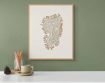 Op de afbeelding: Een beige ingelijst print met een bruin topografisch kaartontwerp en de tekst "Ik hef mijn ogen op naar de bergen waar mijn hulp vandaan komt".