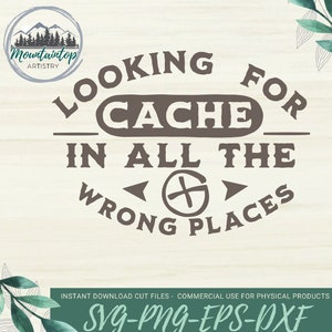 May include: A brown and white graphic design with the text "Looking for Cache in all the wrong places". The graphic includes a compass symbol with arrows pointing left and right. The text "Mountaintop Artistry" is in a circle at the top of the design.