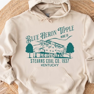 May include: A beige hoodie with a teal blue graphic print of a coal tipple with the text "Blue Heron Tipple Mine 18 Stearns Coal Co. 1937 Kentucky".
