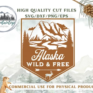 May include: A brown and white graphic design with a mountain range, trees, and a river. The text "Alaska Wild & Free" is in white lettering. The design is in a hexagon shape with a white arrow pointing to the right.