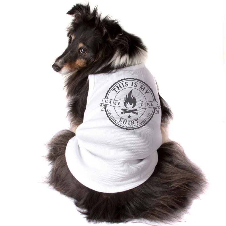 May include: A black, brown, and white dog wearing a white shirt with a black graphic. The graphic reads "THIS IS MY CAMP FIRE SHIRT (IN CASE YOU COULDN'T SMELL IT)" with a campfire illustration. The dog is sitting and looking to the left.