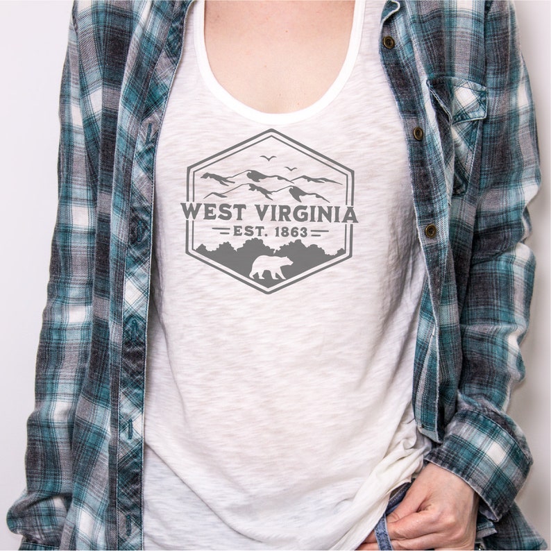 May include: A white tank top with a gray graphic design of a mountain range and a bear. The graphic says "West Virginia - Est. 1863".