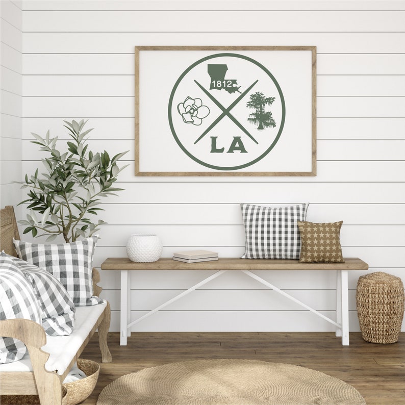 May include: A framed print with a green circle design featuring a magnolia flower, a cypress tree, the state of Louisiana, and the year 1812. The circle is surrounded by the letters "LA".