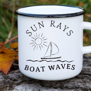 May include: White enamel mug with a black rim. The mug has a black and white illustration of a sailboat on waves with a sun above it. The text "SUN RAYS BOAT WAVES" is printed on the mug.