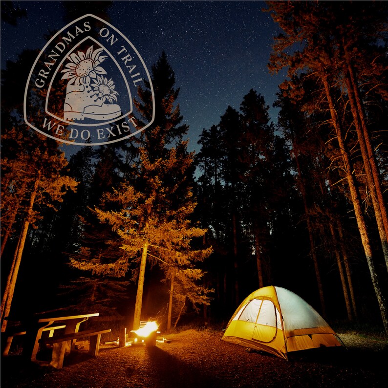 May include: A yellow and white tent is set up in a forest at night. A campfire is burning in front of the tent. The sky is full of stars. A white logo with the text "Grandmas on Trail We Do Exist" is superimposed on the image.