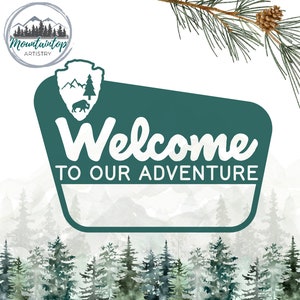 May include: A green sign with a white border and the text "Welcome to our adventure" in a white, stylised font. The sign is in front of a watercolour background of a forest with mountains in the distance.