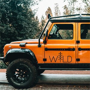 May include: A bright orange off-road vehicle with a black roof rack and a black tire. The vehicle has a "WILD" decal on the side with a stylized pine tree graphic.