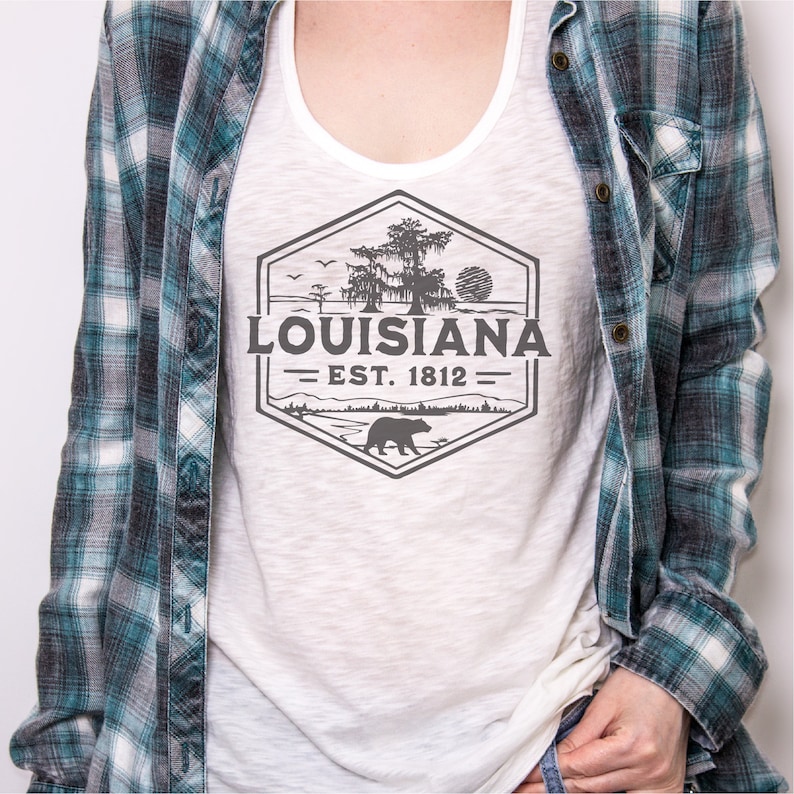 May include: White tank top with a grey graphic design of a hexagon with a tree, a bear, and the text "Louisiana Est. 1812".
