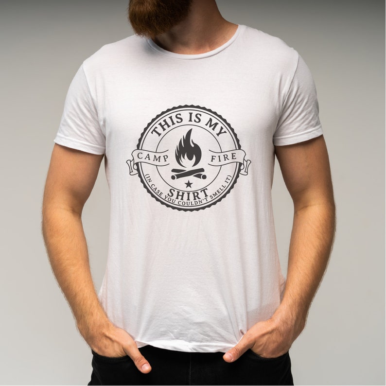 May include: White t-shirt with a black graphic. The graphic is a circular design with the text "THIS IS MY CAMP FIRE SHIRT (IN CASE YOU COULDN'T SMELL IT)" surrounding a campfire illustration.