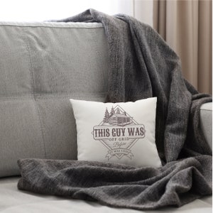 May include: White throw pillow with a brown cabin illustration and the text "This Guy Was Off Grid Before It Was Cool".