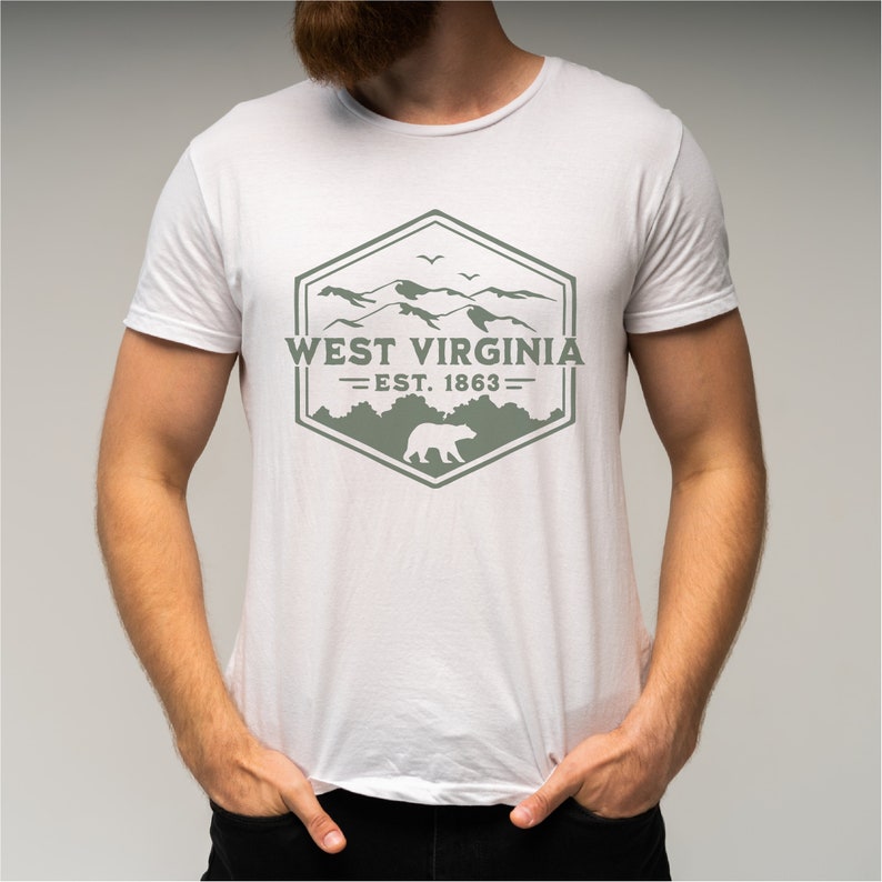 May include: White t-shirt with a green graphic design featuring a mountain range, a bear, and the text "West Virginia - Est. 1863 -"