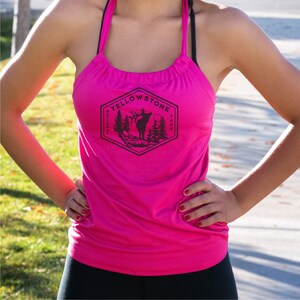 May include: A pink tank top with a black graphic of the Yellowstone National Park logo featuring an elk silhouette and the words "Yellowstone National Park".