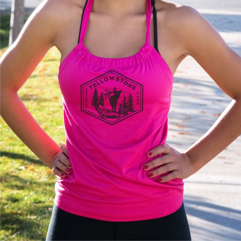 May include: A pink tank top with a black graphic of the Yellowstone National Park logo featuring an elk silhouette and the words "Yellowstone National Park".