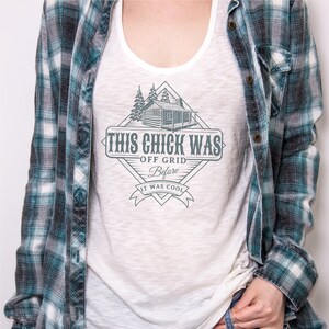 May include: White tank top with a graphic of a cabin in the woods and the text "This Chick Was Off Grid Before It Was Cool".