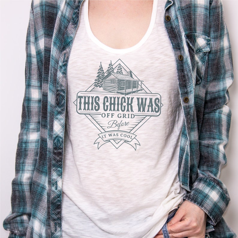 May include: White tank top with a graphic of a cabin in the woods and the text "This Chick Was Off Grid Before It Was Cool".