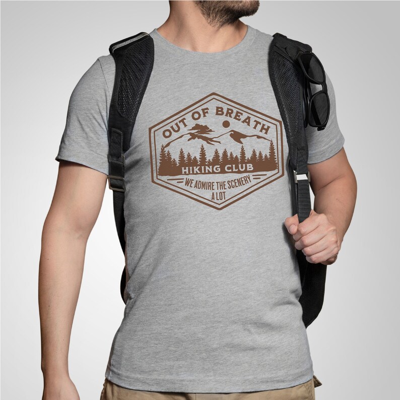 May include: A gray t-shirt with a brown graphic of a mountain range and the text "Out of Breath Hiking Club - We admire the scenery a lot".