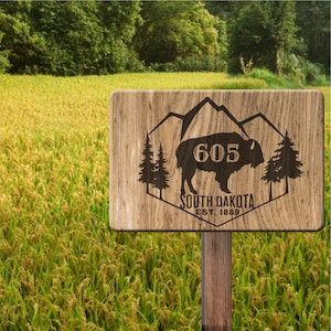 May include: A wooden sign with a brown background and a carved design of a bison with mountains in the background. The sign says "605 South Dakota Est. 1889".
