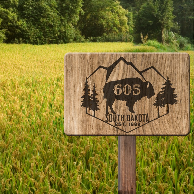 May include: A wooden sign with a brown background and a carved design of a bison with mountains in the background. The sign says "605 South Dakota Est. 1889".
