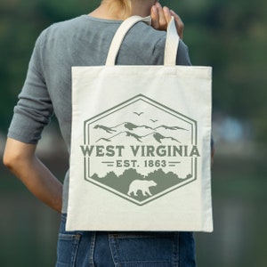May include: A white canvas tote bag with a green logo featuring a mountain range, a bear, and the text "West Virginia - Est. 1863".