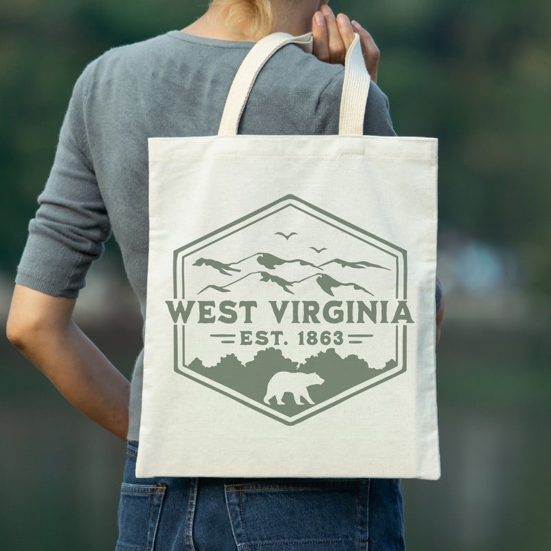 May include: A white canvas tote bag with a green logo featuring a mountain range, a bear, and the text "West Virginia - Est. 1863".