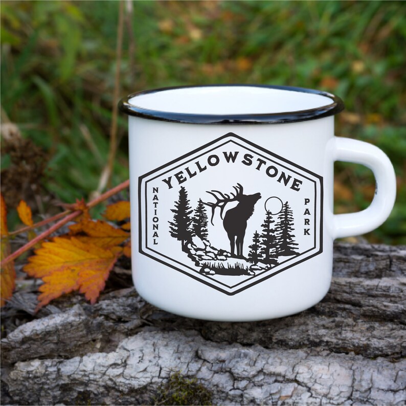 May include: White enamel mug with a black rim and handle. The mug features a black and white graphic of an elk in a forest with the text "Yellowstone National Park".