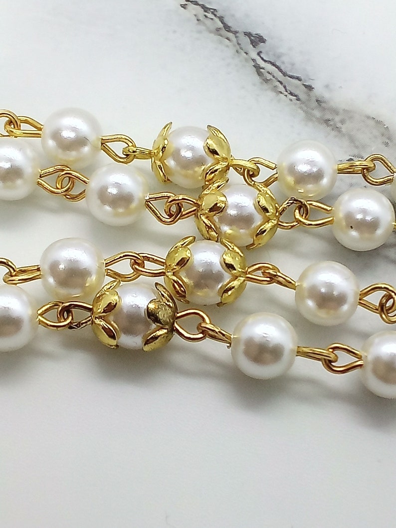 May include: A gold chain necklace with white pearl beads and gold leaf accents.