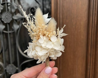 Puede incluir: Un pequeño ramo de hortensias blancas secas y hierba de la pampa beige, atado con cuerda.