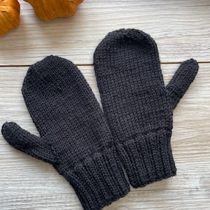 May include: A pair of black knitted mittens. The mittens are made of a soft, warm material and have a simple, classic design.